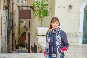 joven hermosa mujer viajera con chaqueta negra mirando a la cámara, sonriendo y posando en la calle de la ciudad de matera foto