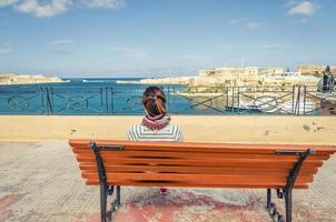 Young girl traveler sit on bench and look away distance at Malta's Grand Harbour photo