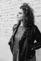 monochrome portrait of young beautiful cheerful woman with curly hair on white bricks wall background. Film stylization photo