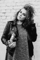 monochrome portrait of young beautiful cheerful woman with red curly hair taking pictures on film old fashioned camera on white bricks wall background. Film stylization photo