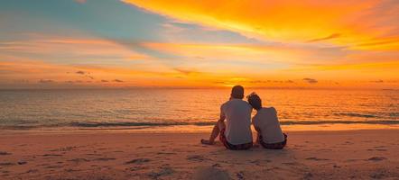 Romantic couple hugging on the beach on sunrise sunset. Honeymoon couple enjoying evening light relaxing on tropical summer vacation travel holiday. Two adults silhouettes lifestyle. photo