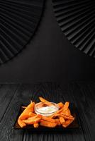 Fried sweet potatoes on a black plate with sauce on a wooden black background. photo