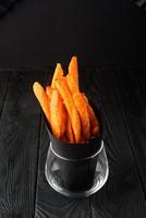 Fried sweet potatoes on a black plate with sauce on a wooden black background. photo