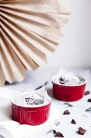 Chocolate muffins in red cups. Small glazed ceramic ramekin with brown cakes on a gray and white background. photo