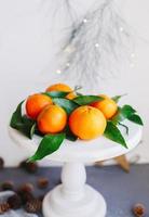 Orange tangerines on grey background in New Year's decor with brown pine cones and green leaves. Christmas decoration with mandarins. Delicious sweet clementine. photo