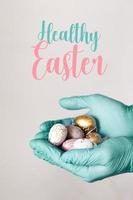 Hands in medical gloves holding modern painted easter eggs. Selective focus. Toned picture. Isolated.Healthy Easter text photo