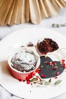 muffin de chocolate en taza roja. maqueta de san valentín corazón negro copyspace. pequeño ramekin de cerámica vidriada con pastel marrón sobre fondo blanco. foto