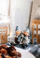 Porcelain figurines of children in a Christmas decor. Winter figurines of a boy and a girl with gifts on the background of houses and cones. Christmas Greeting Card. Copy space. photo