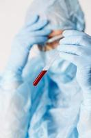 Close up of doctor hand holding blood sample. Medical equipment. Blood test. A doctor wearing personal protective equipment including mask, goggle, and suit to protect COVID-19 coronavirus infection. photo