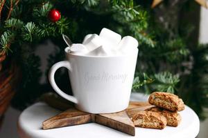 café en una taza blanca con malvaviscos. café festivo matutino con galletas de almendra cantuccini italianas tradicionales. una taza de café sobre un fondo de ramas de abeto verde sobre un soporte blanco. foto