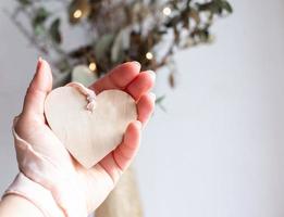 Light wooden heart on a silk pink ribbon on white background. Space for text. Hand holding a wooden heart pendant on a chiffon pale pink ribbon. Copy space. photo