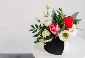 copyspace de corazón de tablero negro. ramo de primavera en jarrón blanco sobre soporte blanco de madera. rosas, tulipanes y lisianthus. foto