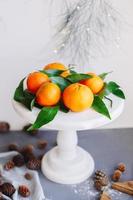 Orange tangerines on grey background in New Year's decor with brown pine cones and green leaves. Christmas decoration with mandarins. Delicious sweet clementine. photo