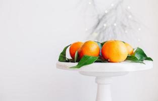 Orange tangerines on grey background in New Year's decor with brown pine cones and green leaves. Christmas decoration with mandarins. Delicious sweet clementine. photo