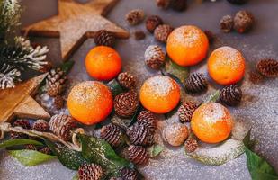 Orange tangerines on grey background in New Year's decor with brown pine cones and green leaves. Christmas decoration with mandarins. Delicious sweet clementine. photo