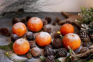 Orange tangerines on grey background in New Year's decor with brown pine cones and green leaves. Christmas decoration with mandarins. Delicious sweet clementine. photo