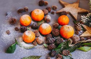 Orange tangerines on grey background in New Year's decor with brown pine cones and green leaves. Christmas decoration with mandarins. Delicious sweet clementine. photo