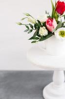 Spring bouquet in white vase on wooden white stand. Roses, tulips and lisianthus. photo