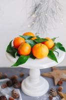 Orange tangerines on grey background in New Year's decor with brown pine cones and green leaves. Christmas decoration with mandarins. Delicious sweet clementine. photo