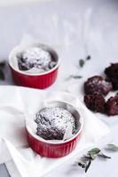 Chocolate muffins in red cups. Small glazed ceramic ramekin with brown cakes on a gray and white background. photo