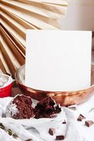 Chocolate muffins in red cups. Mockup white paper copyspace. Small glazed ceramic ramekin with brown cakes on a gray and white background. photo