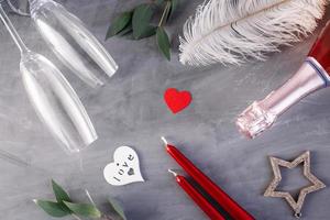 Flat lay composition with bottle of champagne, candles, feather and hearts for celebration on grey concrete background. Glass for champagne. photo