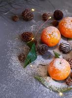 Orange tangerines on grey background in New Year's decor with brown pine cones and green leaves. Christmas decoration with mandarins. Delicious sweet clementine. photo