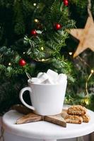 Coffee in a white cup with marshmallows. Morning festive coffee with traditional Italian cantuccini almond cookies. A cup of coffee on a background of green fir branches on a white stand. photo