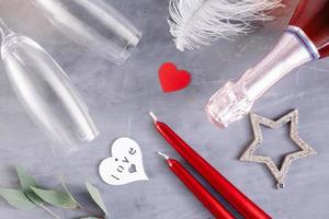 Flat lay composition with bottle of champagne, candles, feather and hearts for celebration on grey concrete background. Glass for champagne. photo