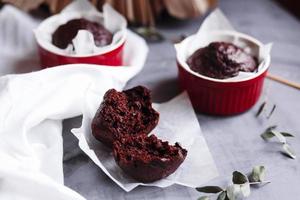 Chocolate muffins in red cups. Small glazed ceramic ramekin with brown cakes on a gray and white background. photo