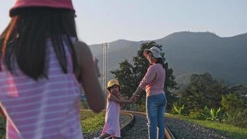 två söta asiatiska tjejer springer tillsammans på järnvägsspår på landsbygden mot bergen på kvällen. video