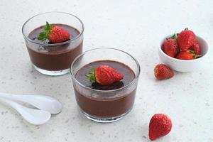 pudín de chocolate con fresas en vaso sobre mesa blanca. foco seleccionado. foto