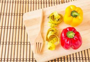 Yellow tape measure and sweet red pepper on wooden plate. photo