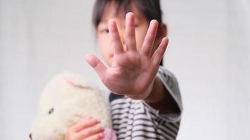 Cute little girl hugging a doll and making stop gesture on white background. Stop violence against children and child abuse problem. video