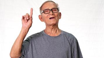 homme âgé excité et souriant pointant vers le haut sur un espace vide sur fond de studio blanc. video