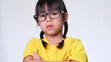 uma menina chateada com óculos fica com os braços cruzados e olha para a câmera em um fundo de estúdio branco. video