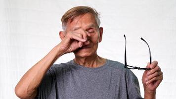 Old man with eye fatigue holding eyeglasses on white background in studio. video