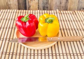 Yellow red bell pepper and knife in wooden plates photo