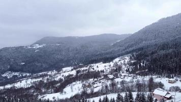 vista aérea de drones de belas paisagens de inverno nas montanhas com pinheiros cobertos de neve. céu escuro e neve caindo. pequena aldeia abaixo da montanha. tiro cinematográfico. viagem de inverno.
