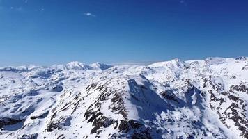 Aerial drone of an amazing panoramic view of a mountain range covered with snow during a sunny day. Winter season and holidays in the mountains. Blue sky and white vibrant colors. Cinematic shot. video