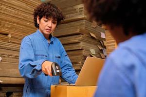 Two safety uniform female workers and colleagues use bar code scanner to check shipment orders stock at parcels warehouse, paper manufacture factory for packing industry, logistic transport service. photo