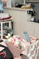 florist in a flower shop holding a bouquet and texting to a client. small business, flowers delivery, working space. photo