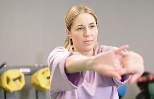 woman stretching her arms in a gym, warming up before training, workout in fitness club, real people. healthy lifestyle. photo