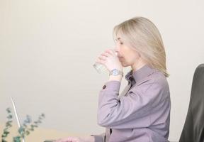mujer sedienta en la oficina bebiendo agua durante la jornada laboral. piel humudufiing e hidratación. trabajo de oficina. mujer empleada rubia., espacio de copia foto