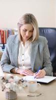 left handed woman boss writing in a notebook planning working day. employer woman wearing formal chothes in office working in the morning. vertical shot photo
