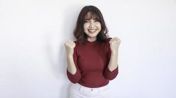 feliz y ganadora hermosa chica asiática con camisa roja en fondo blanco foto