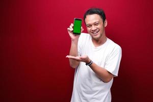 Smile Young Asian man pointing on green blank space on smartphone on red background. photo