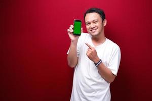 Smile Young Asian man pointing on green blank space on smartphone on red background. photo