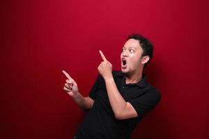 Young asian man is surprised and shouting wow with pointing right with his hand isolated on red background. photo