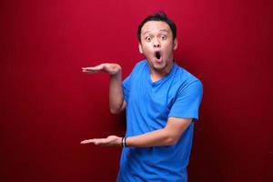 Young asian man is surprised and shouting wow with pointing right with his hand isolated on red background. photo